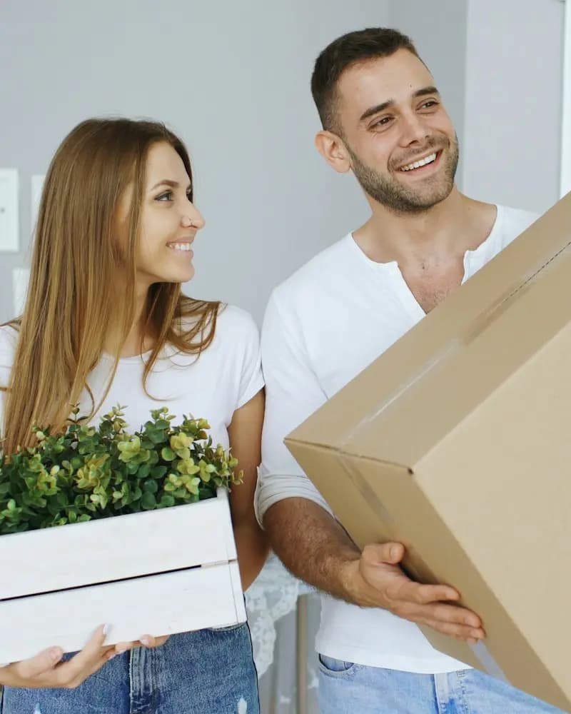 Beispielbild: Paar trägt Umzugskarton und Pflanze ins neue Zuhause